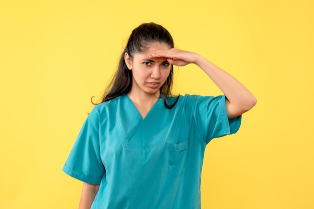 Vue de face de la jolie femme médecin regardant quelque chose sur le mur jaune