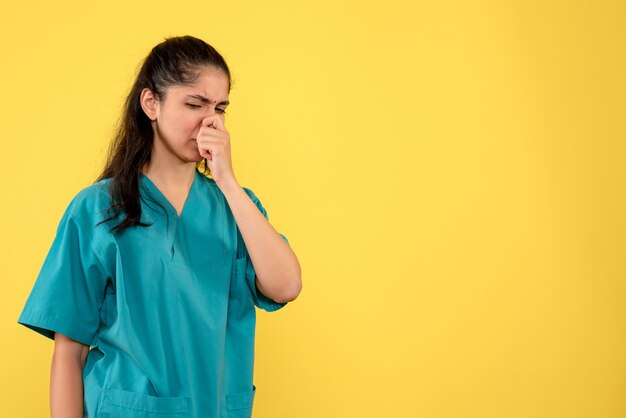 Vue de face de la jolie femme médecin tenant son nez sur le mur jaune