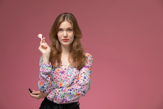 Vue de face jolie femme posant avec son pinceau à poudre cosmétique