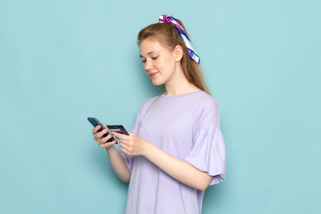 Une vue de face jolie femme en robe-chemise bleue tenant et à l'aide d'un téléphone sur bleu