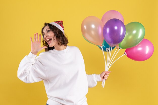 Vue de face jolie femme tenant des ballons colorés sur jaune