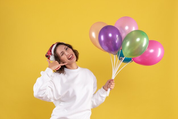 Vue de face jolie femme tenant des ballons colorés sur jaune