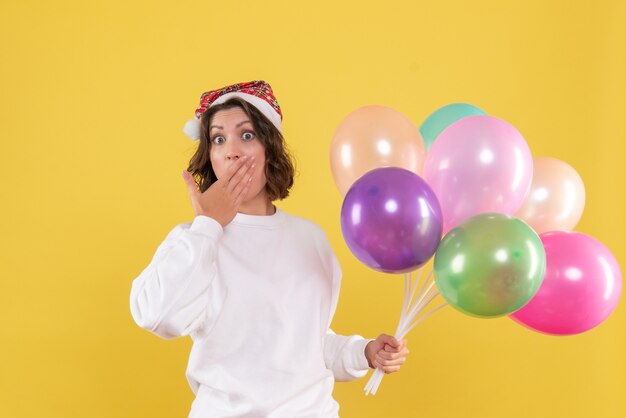 Vue de face jolie femme tenant des ballons colorés sur jaune