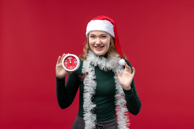 Vue de face jolie femme tenant horloge sur le fond rouge