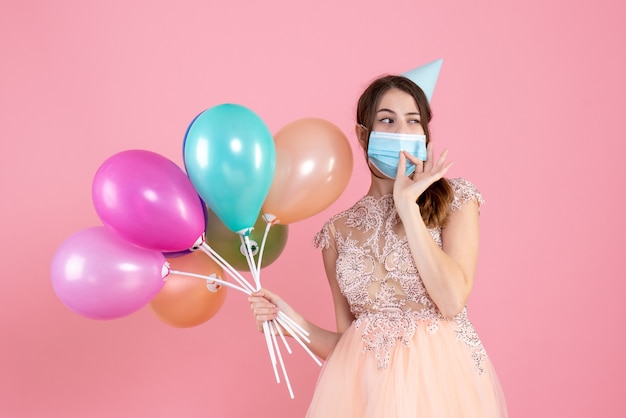 Vue de face jolie fêtarde avec chapeau de fête tenant des ballons colorés