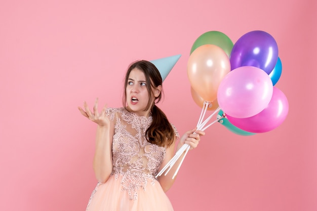 Vue de face jolie fêtarde avec chapeau de fête tenant quelque chose de ballons