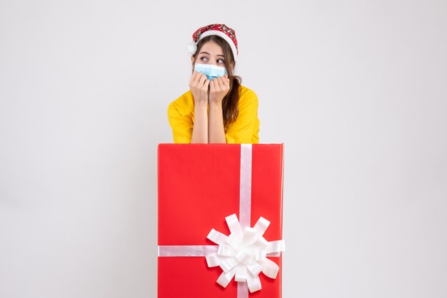 Vue de face jolie fille de Noël avec bonnet de Noel debout derrière un grand cadeau de Noël