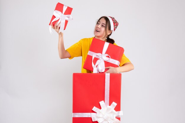 Vue de face jolie fille de Noël avec bonnet de Noel tenant des cadeaux debout derrière un grand cadeau de Noël