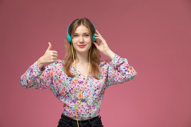 Vue de face jolie jeune femme avec casque et montre les pouces vers le haut sur le mur rose foncé