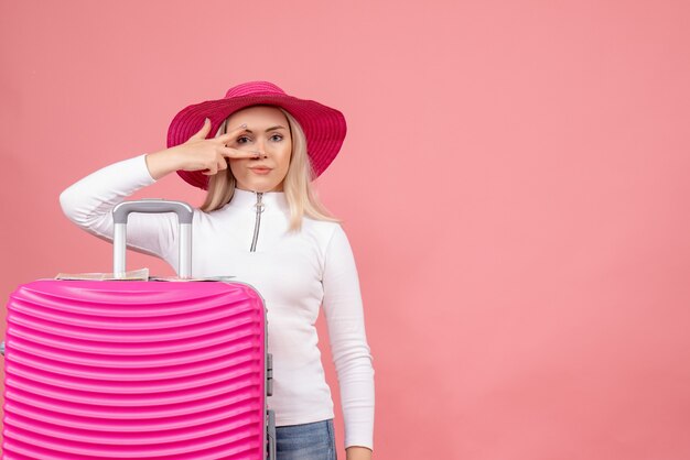 Vue de face jolie jeune femme debout derrière une valise rose