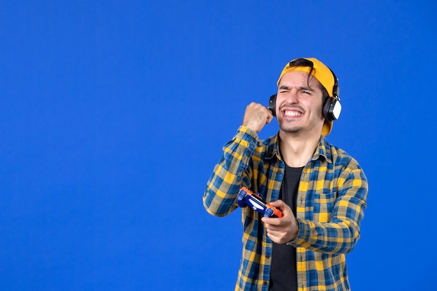 Vue de face d'un joueur masculin avec une manette de jeu jouant à un jeu vidéo sur un mur bleu