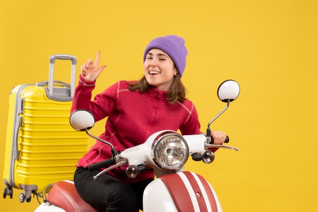 Vue de face joyeuse jeune femme sur le doigt pointé du cyclomoteur vers le haut