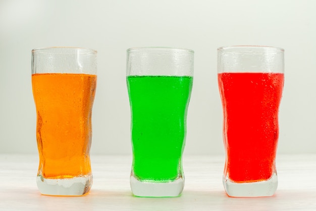 Vue de face jus colorés à l'intérieur de longs verres sur une surface blanche