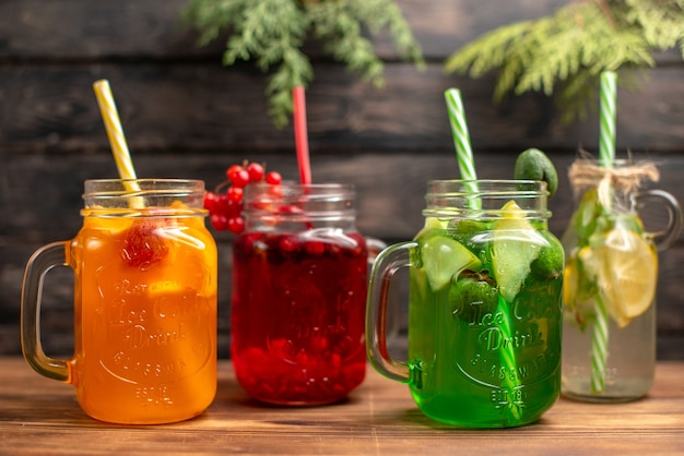 Vue de face de jus de fruits frais biologiques en bouteilles servis avec des tubes et des fruits sur un fond en bois marron