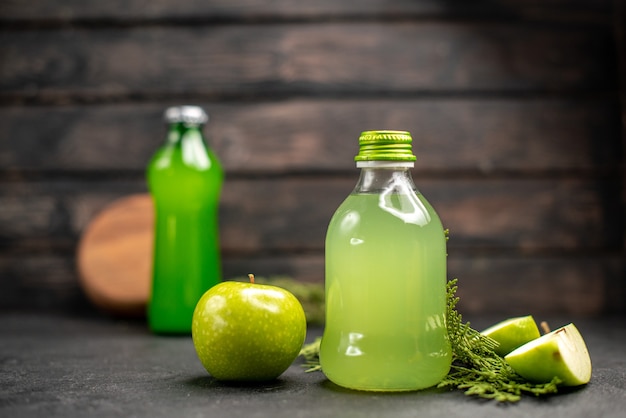 Vue de face jus de pomme en bouteille pomme pomme coupée bouteille verte sur une surface isolée en bois