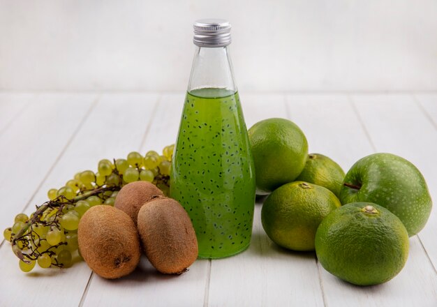 Vue de face kiwi avec une bouteille de jus de raisins et de mandarines sur un mur blanc