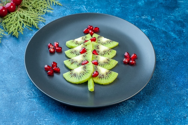 Vue de face de kiwis frais tranchés avec des grenades à l'intérieur de la plaque sur une surface bleue jus moelleux couleur fruit photo tropical exotique