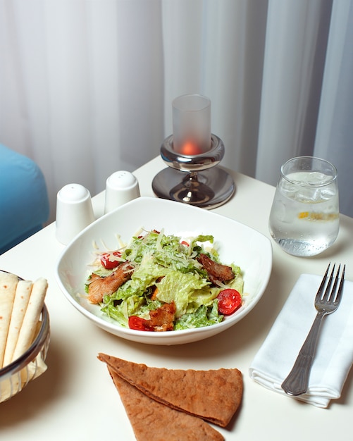 Photo gratuite une vue de face des légumes cuits à l'intérieur de la plaque blanche avec de la cultery et des tranches de pain sur le tableau blanc