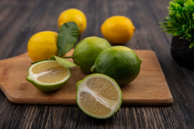 Vue de face limes coupées en deux sur une planche à découper avec des citrons sur un fond en bois