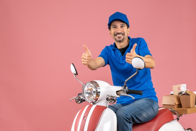 Vue De Face D'un Livreur Heureux Portant Un Chapeau Assis Sur Un Scooter Faisant Un Geste Ok Sur Fond De Pêche Pastel