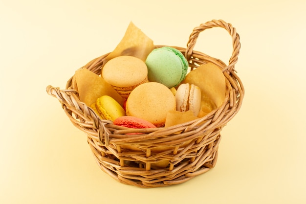 Une vue de face macarons français colorés à l'intérieur du panier sur le bureau jaune gâteau biscuit sucre sucré