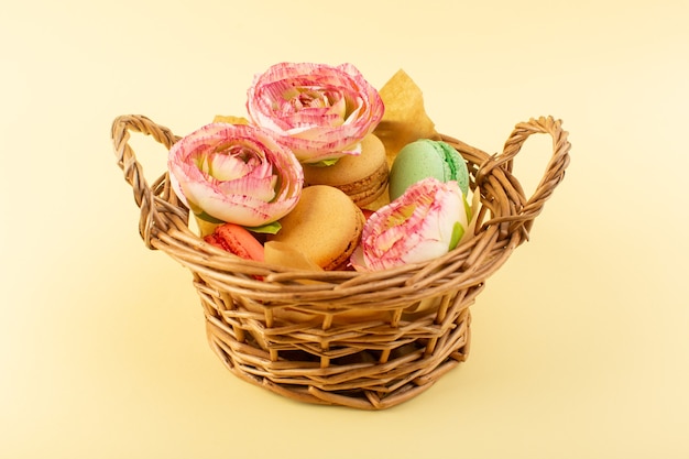 Une vue de face macarons français avec des fleurs à l'intérieur du panier sur le bureau jaune gâteau biscuit sucre sucré