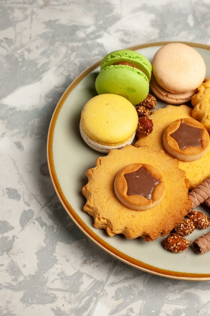 Photo gratuite vue de face macarons français avec des gâteaux et des cookies sur une surface blanche