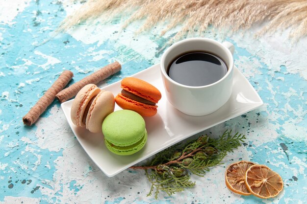 Vue de face macarons français avec tasse de thé sur la surface bleue