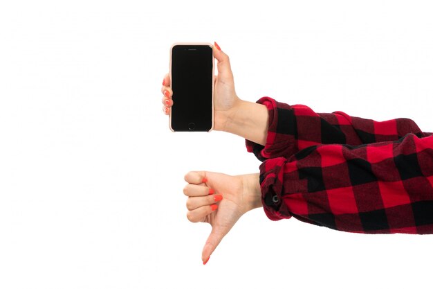 Une vue de face de la main féminine en chemise à carreaux noir-rouge holding smartphone montrant pas cool signe sur le blanc