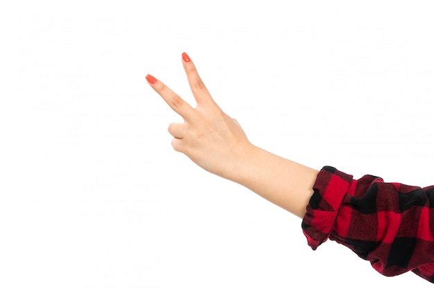 Une vue de face de la main féminine en chemise à carreaux noir-rouge montrant le signe de la victoire sur le blanc