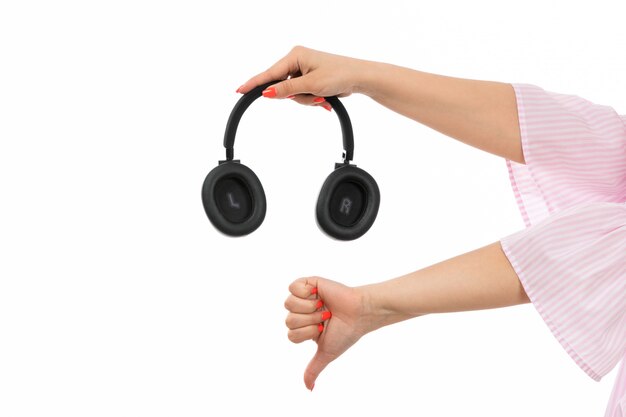 Une vue de face main féminine tenant des écouteurs noirs montrant un signe différent sur le blanc