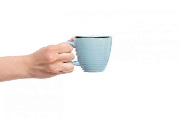 Une vue de face main féminine tenant une petite tasse bleue sur le blanc