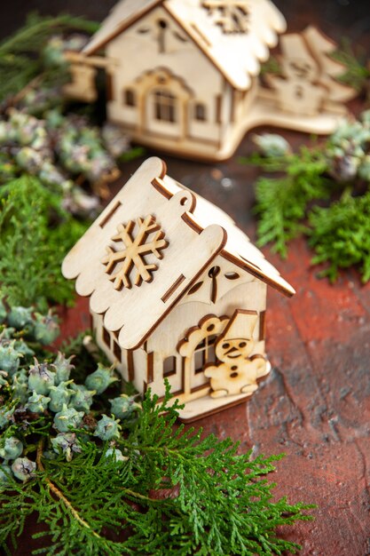 Vue de face des maisons de jouets en bois branches de pin sur une table rouge foncé