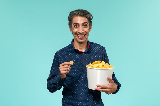 Vue de face mâle d'âge moyen manger cips et rire sur la surface bleue