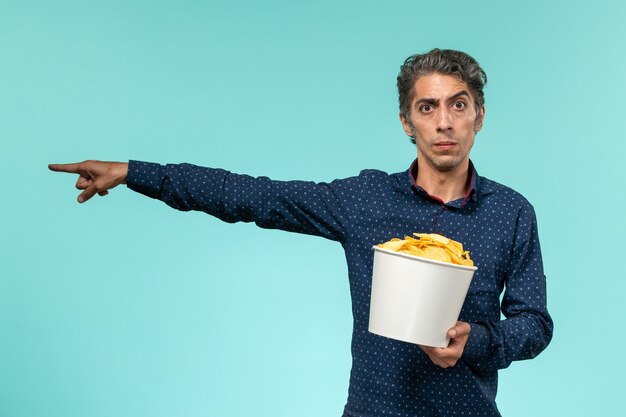 Vue de face mâle d'âge moyen tenant des cips de pommes de terre sur le bureau bleu