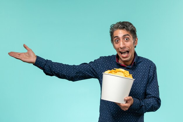 Vue de face mâle d'âge moyen tenant panier avec cips sur bureau bleu