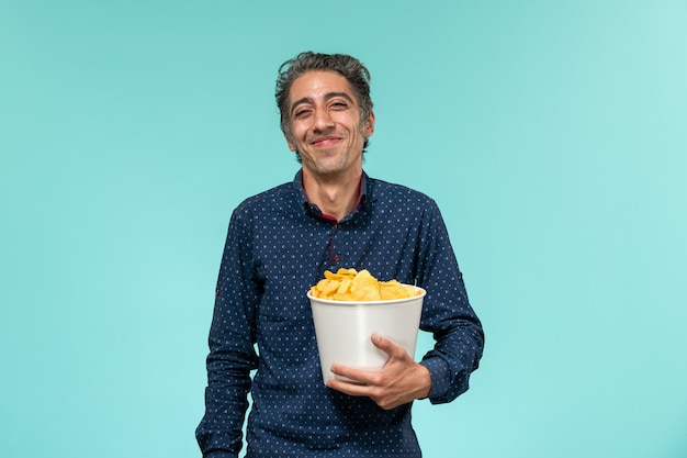 Vue de face mâle d'âge moyen tenant panier avec cips sur bureau bleu