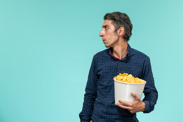 Vue de face mâle d'âge moyen tenant panier avec cips sur la surface bleue