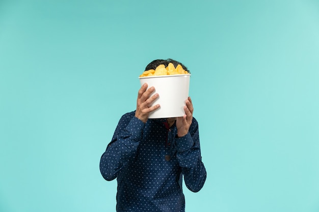 Vue de face mâle d'âge moyen tenant panier avec cips sur la surface bleue