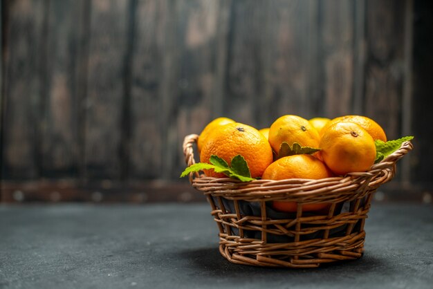 Vue de face des mandarines fraîches dans un panier en osier sur un endroit sombre et libre