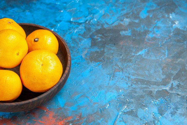 Vue de face des mandarines fraîches à l'intérieur de la plaque sur la table bleue