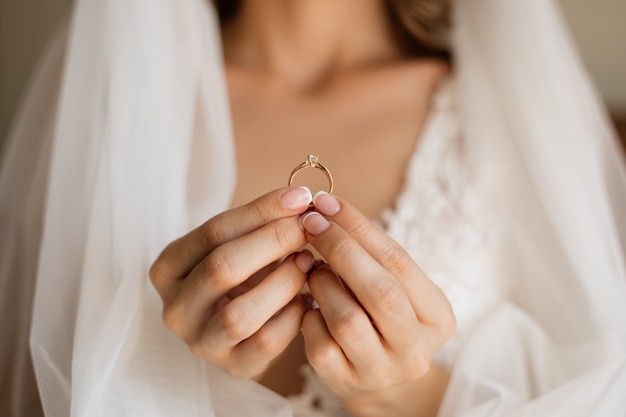 Vue de face de la mariée tient une précieuse bague de fiançailles dans les mains devant la poitrine et le voile de mariage