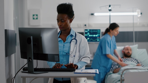 Vue de face d'un médecin afro-américain tapant une expertise médicale sur ordinateur