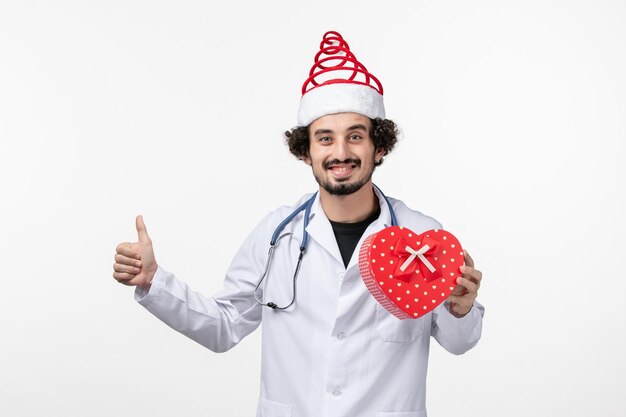 Vue de face d'un médecin de sexe masculin avec un cadeau de vacances sur un mur blanc
