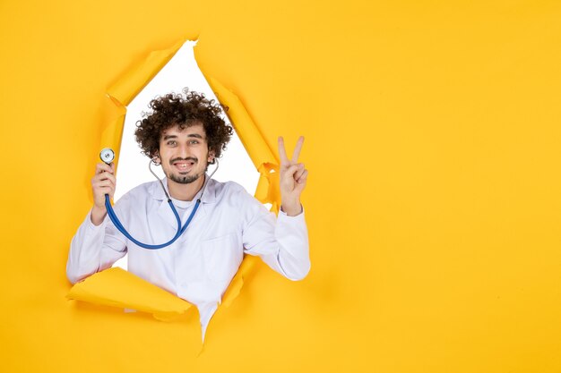 Vue de face médecin de sexe masculin en costume médical blanc avec stéthoscope sur le virus de la médecine de la santé de l'hôpital médical de couleur jaune déchiré