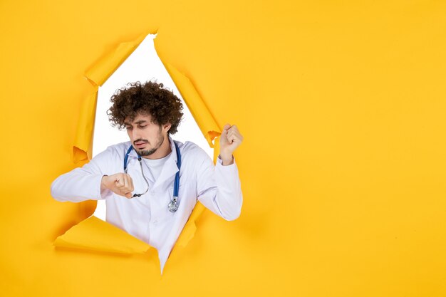 Photo gratuite vue de face médecin de sexe masculin en costume médical blanc vérifiant l'heure sur un hôpital médical de couleur de virus de médecine de santé déchiré jaune