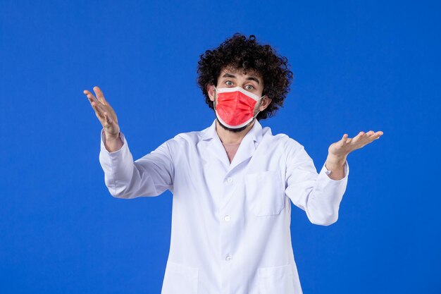 Vue de face d'un médecin de sexe masculin en costume médical et masque sur fond bleu vaccin contre virus de la santé pandémique médicament hospitalier