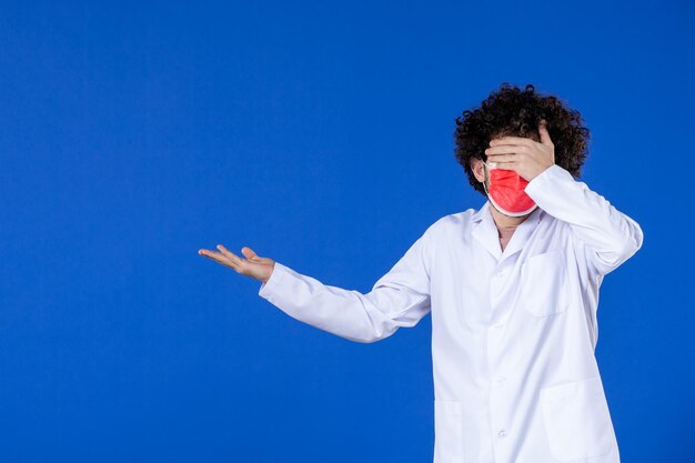 Vue de face d'un médecin de sexe masculin en costume médical et masque sur fond bleu vaccin covid- virus de la médecine de la santé hôpital médicament pandémique couleur