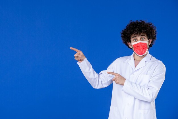 Vue de face d'un médecin de sexe masculin en costume médical et masque sur une surface bleue