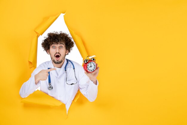 Vue de face médecin de sexe masculin en costume médical tenant des horloges sur l'heure de la médecine médicale de l'hôpital de couleur jaune